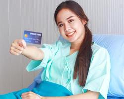 vacker asiatisk kvinna med ett kreditkort sitter i en sjukhussäng med ett leende ansikte foto