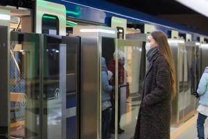 en flicka i en kirurgisk ansiktsmask håller socialt avstånd på en tunnelbanestation foto
