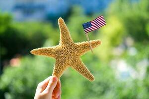sjöstjärna innehar de amerikan flagga på en suddig grön bakgrund. arbetskraft dag Semester begrepp. 4:e av juli USA oberoende dag. kopia Plats för text. foto