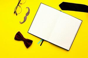 platt lägga mustasch, glasögon, rosett slips och slips på en gul bakgrund. attrapp manlig dagbok. mannens skrivbord foto