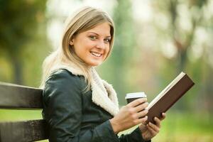 en kvinna har kaffe i de parkera och läsning en bok foto