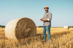 en jordbrukare är stående bredvid balar av hö foto