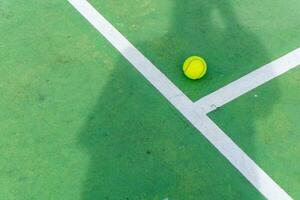 gul tennis boll på grön domstol och vit rader. tennis spelare skugga på domstol på solig dag foto