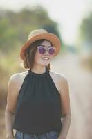 skön asiatisk kvinna bär sugrör hatt toothy leende med lycka stående utomhus- mot skön morgon- ljus foto