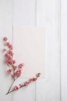 tom papper kort attrapp och rosa körsbär blomma gren platt lägga på vit trä- tabell topp, generativ ai. foto