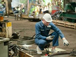 man manlig person människor vit Färg Hardhat hjälm blå Färg enhetlig säkerhet sitta se smartphone mobil teknologi elektronisk forskning arbete jobb ockupation tekniker ingenjör fabrik tillverkning foto