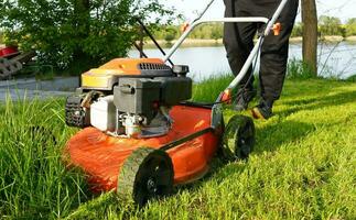 gräsmatta gräsklippning. person klippning de gräs med orange gräsklippare. klippning i de sommar på solig dag. foto