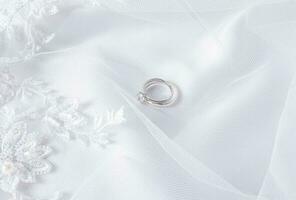 två bröllop ringar tillverkad av vit guld med en diamant lögn på en vit slöja med mjuk veck. bröllop bakgrund. layout för design. vykort. inbjudan. foto