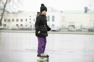 de flicka går skridskoåkning i de vinter- mot de bakgrund av de stad. foto