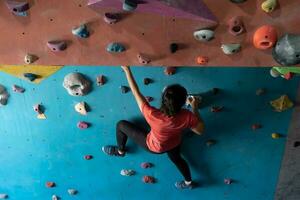 kvinna klättrande på vägg Träning i Gym, aktiva sportig kvinna praktiserande sten klättrande på artificiell sten i extrem sport, bouldering, vägg, klättrare är Träning, sten klättrande i de stad, stark foto
