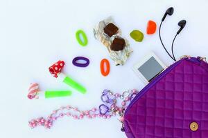 barns handväska och Tillbehör mobil telefon, vissla, hår band, godis, pärlor, hörlurar på vit bakgrund. topp se. foto