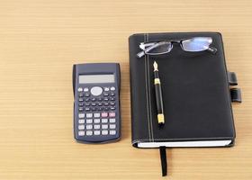 miniräknare och affärsbok med reservoarpenna och glasögon på träskrivbordet foto