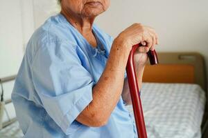 asiatisk äldre handikapp kvinna patient innehav gående pinne i rynkig hand på sjukhus. foto