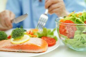 asiatisk äldre kvinna patient äter lax insats och vegetabiliska sallad för friska mat i sjukhus. foto