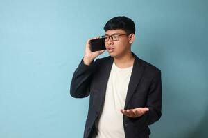 porträtt av ung asiatisk företag man i tillfällig kostym argumenterar med någon på de telefon. isolerat bild på blå bakgrund foto