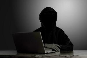mystisk man bär svart luvtröja använder sig av bärbar dator i de mörk rum. hacker och cyber säkerhet begrepp. foto