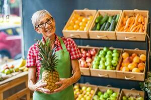 mogna kvinna Arbetar i frukt och grönsaker affär. hon är innehav ananas. foto