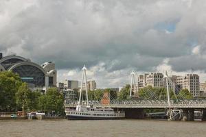utsikt över de gyllene jubileumsbroarna och Charing Cross Station från södra stranden av Themsen i London på en molnig sommardag foto