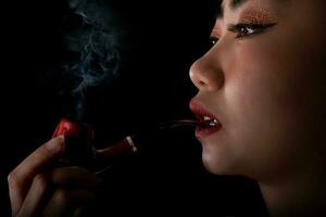 stående vacker asiatisk ung kvinna med en rökpiptobak på en svart bakgrund