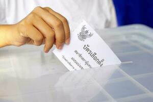 thai människor släppa deras valsedel papper in i de låda till rösta för medlemmar av de hus av representanter. de valsedel papper är skriven i thai, menande val på en valkrets grund valsedel papper foto