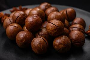utsökt rostad macadamia nötter i skal på en mörk texturerad bakgrund foto
