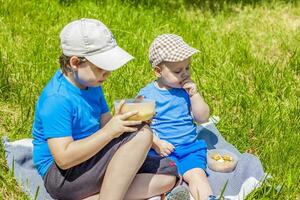 sommar och en värma dag. barn på en picknick sitta på en filt och äta frukt från en tallrik. leva känslor av de killar. foto