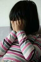 en upprörd barn flicka omslag henne ansikte med hand foto