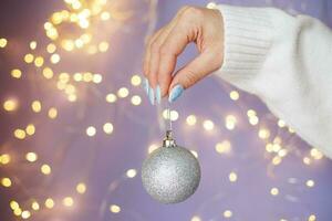 kvinnors händer med naglar innehav jul leksak boll på en lila festlig suddig bokeh bakgrund foto