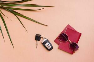ljus resa platt lägga med solglasögon, pass, handflatan löv och bil nycklar på en beige bakgrund. bil resa. topp se foto