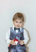 en liten pojke innehar och händer över en röd låda, en hjärtans dag tema begrepp. porträtt av en söt pojke i en kostym med en rosett slips. hjärtans dag. foto