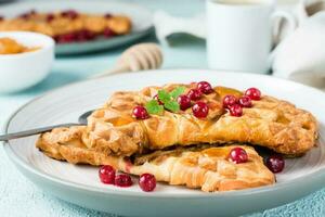 Krispig croissant våfflor med röd vinbär, honung och mynta på plattor och en kopp av kaffe på en ljus tabell. ljuv aptitretande frukost - croffels. närbild foto