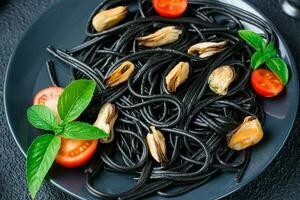 klar att äta svart spaghetti med musslor, tomater och basilika på en tallrik på en svart bakgrund. mat fotografi i mörk färger. närbild foto