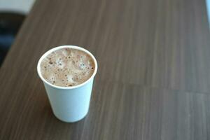 kakao mjölk papper kopp innehav i kvinna hand med brun trä- tabell i Kafé foto