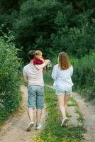 Lycklig ung familj med deras son i deras vapen är gående längs en skog väg och njuter de sommar väder foto