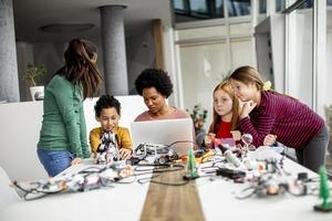 glada barn med sin afroamerikanska kvinnliga naturvetenskapslärare med bärbar dator som programmerar elektriska leksaker och robotar i klassik för robotik