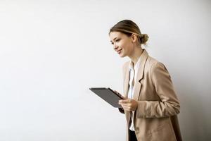ung kvinna som rymmer den digitala minnestavlan vid den vita väggen i modernt kontor