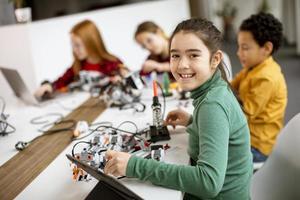 glada barn som programmerar elektriska leksaker och robotar i klassrummet för robotik foto