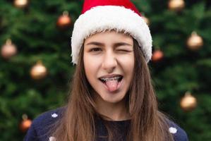 närbild porträtt av kvinna som bär en jultomten hatt med känslor sticker tungan ut