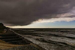 havet landskap med vatten vågor, strand och hotande mörk hotfull storm moln i vår foto