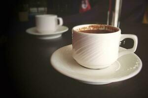 liten vit kopp med varm svart kaffe på en brun tabell foto