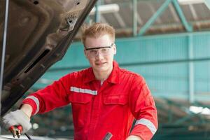 tekniker man med laddning kablar för bil batteri, bil mekaniker arbetssätt i garage, tekniker arbetssätt i bil service, bil reparera, och underhåll foto