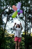 Lycklig barn flicka spelar med färgrik leksak ballonger i de parkera utomhus. foto