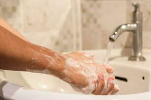närbild av man tvättning händer med tvål över handfat i badrum. hygien behandling foto