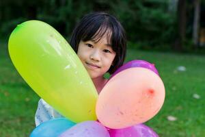 barn flicka innehav färgrik leksak ballonger i de parkera utomhus. foto
