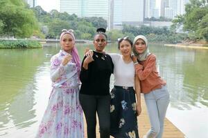 grupp av kvinna malaysiska kinesisk indisk asiatisk utomhus- grön parkera sjö natur Lycklig stå leende blanda gest foto