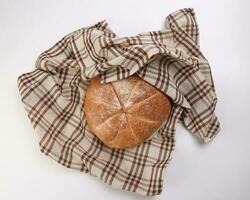 färsk bakad runda bröd limpa insvept i rutig kök tyg servett handduk över vit bakgrund foto