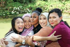 grupp av fem kvinna vänner malaysiska kinesisk indisk asiatisk utomhus- parkera sjö natur kramas omtänksam skrattande Lycklig foto