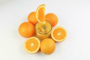 färsk gul orange juice i glas med hela flytande skivad orange frukt och is kub på vit bakgrund foto