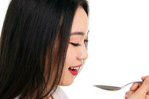 skön ung söder öst asiatisk kvinna låtsas verkande Framställ innehav tömma sked i hand på mun äta smak slicka vit bakgrund tillfredsställelse smaskigt foto