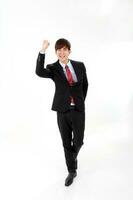 ung smart stilig asiatisk man företag kontor bär kostym slips på vit bakgrund se på kamera promenad framåt- näve upp glädje Framgång foto
